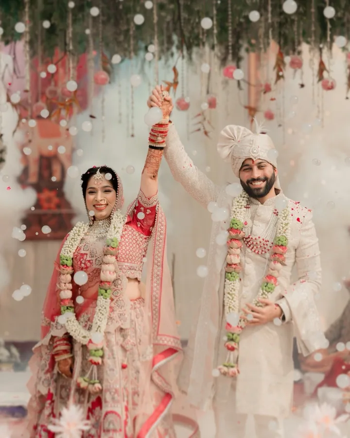 Bride and groom raising joined hands amid falling petals