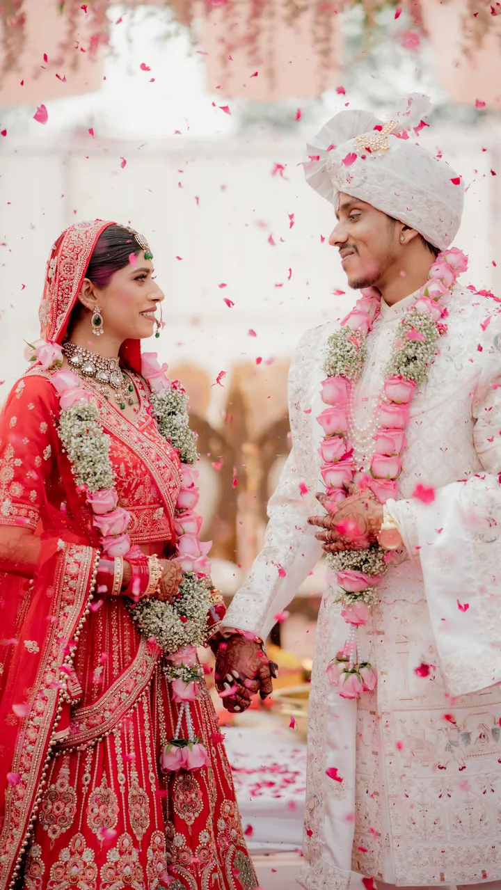 Bride and groom exchanging garlands under falling petals